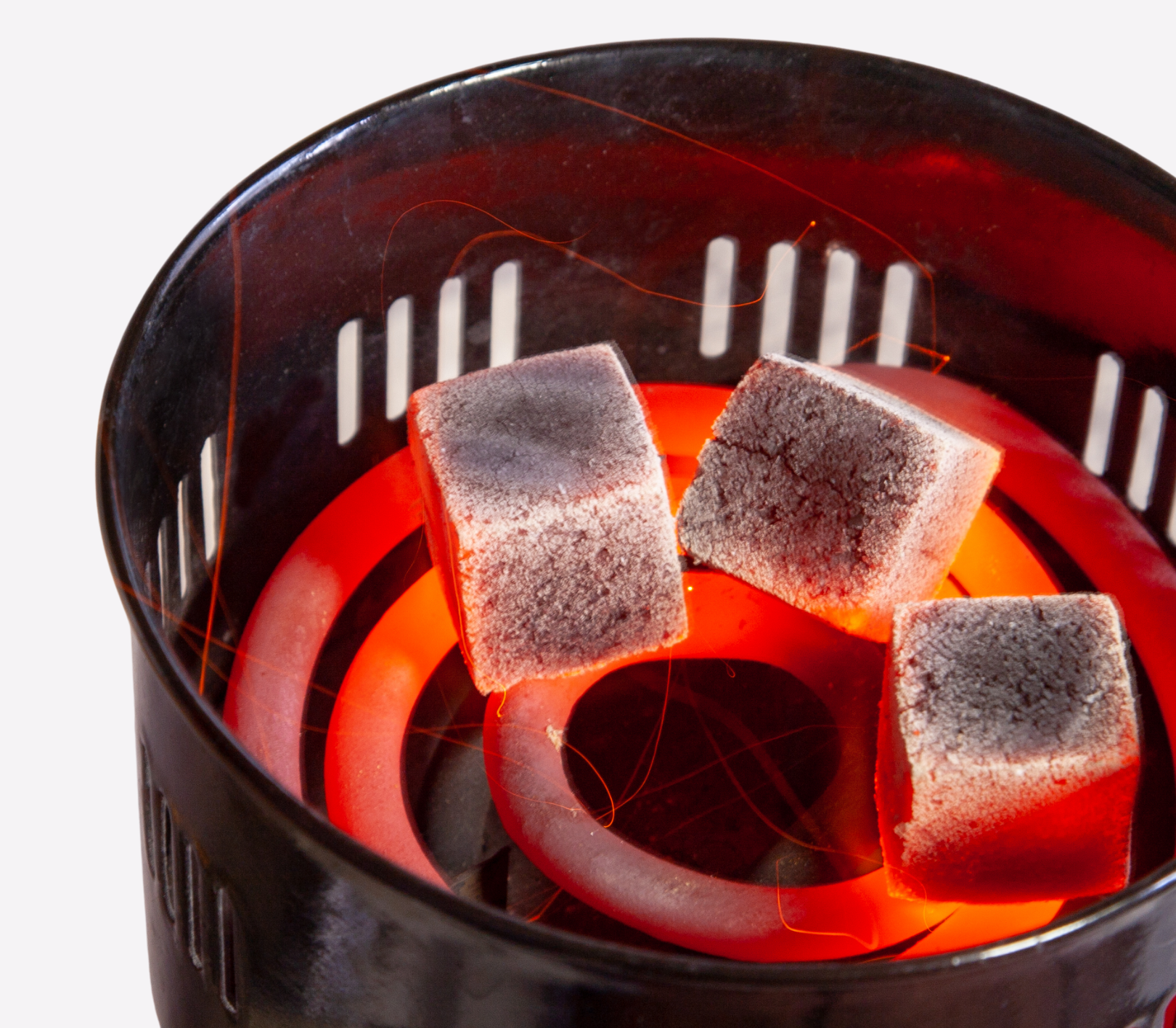 Three charcoal briquettes on a lit barbecue grill with a white background