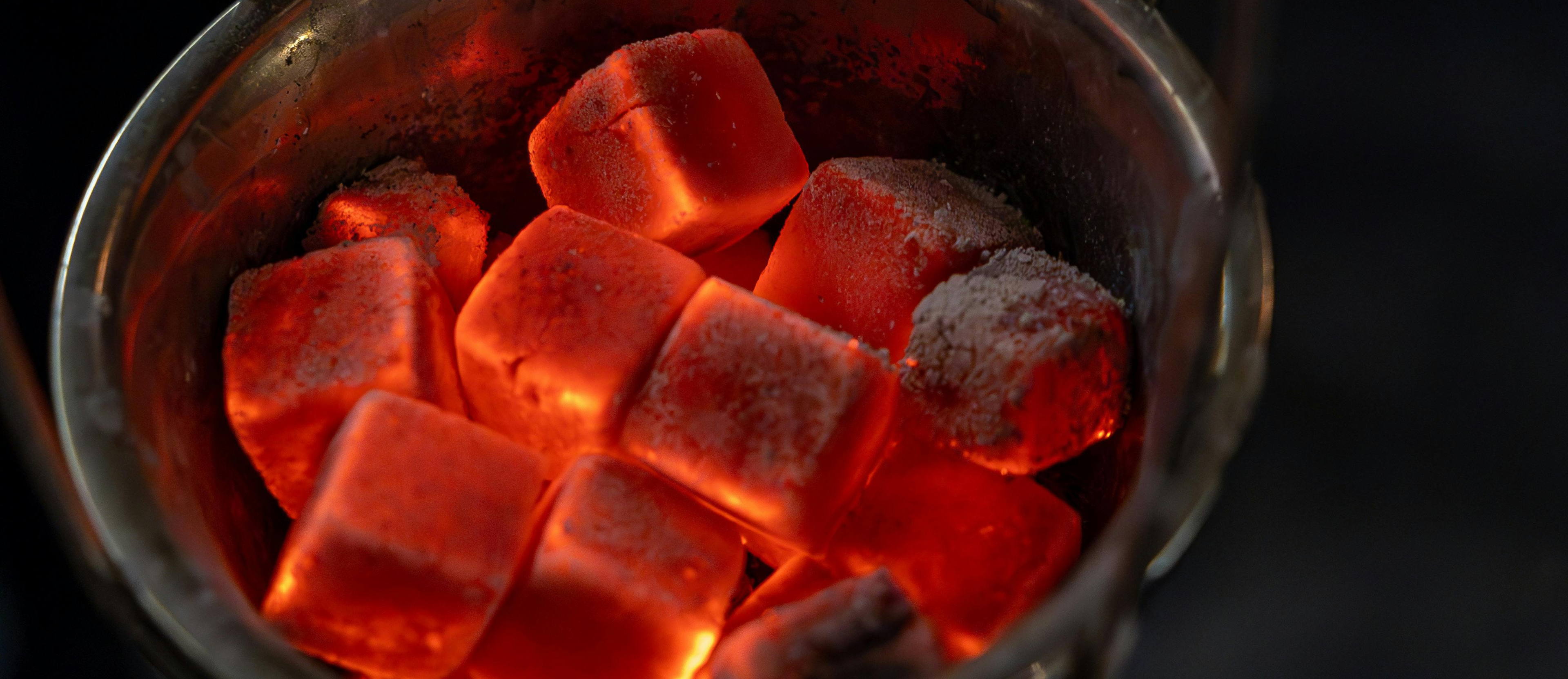 Metal container filled with glowing red-hot charcoal briquettes on a dark background
